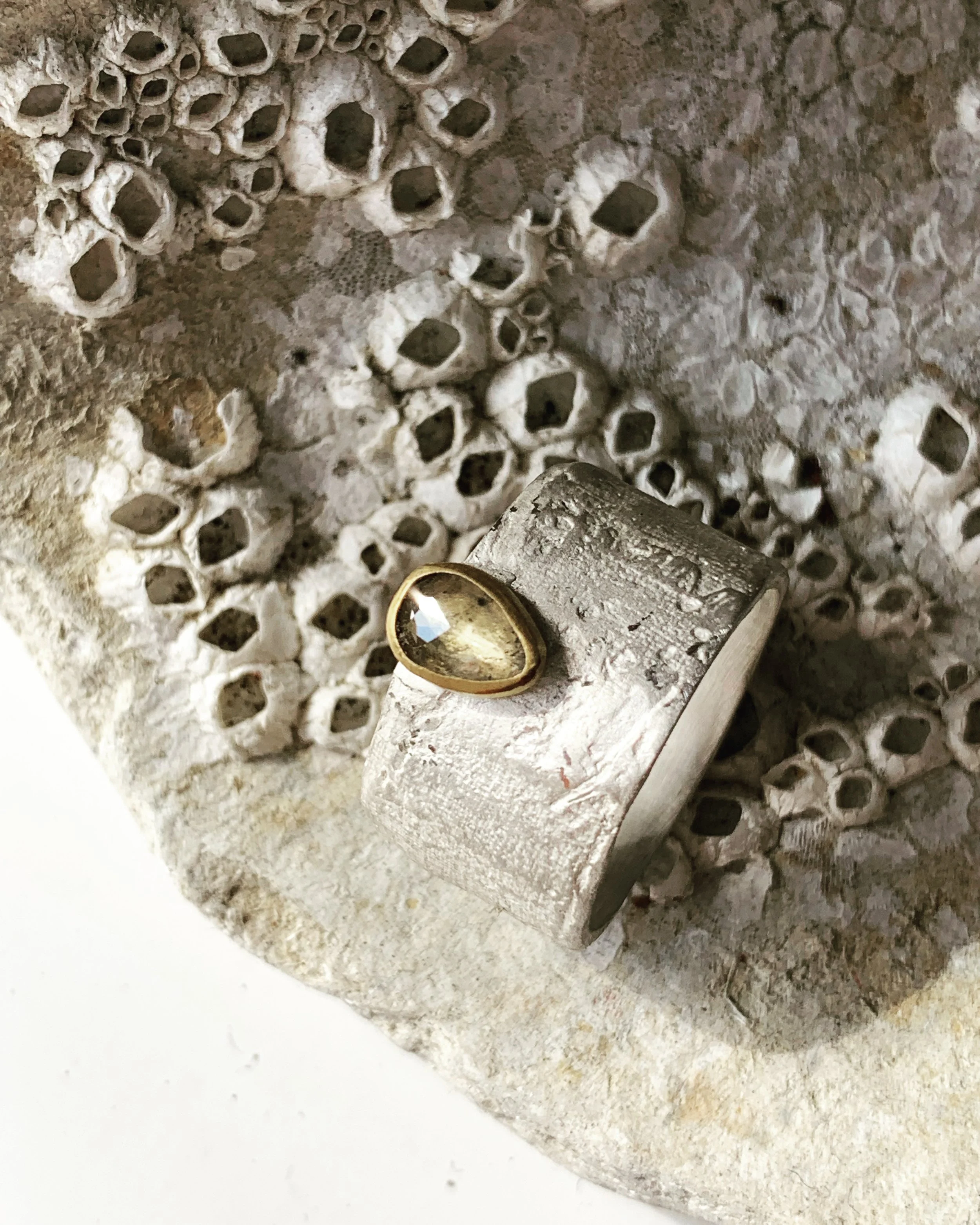 Close-up of a decorative object with a textured, honeycomb pattern background and a silver band with a large, tear-shaped clear gemstone set into it.