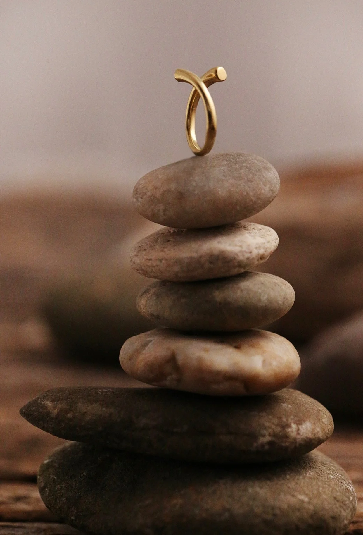 A stack of smooth, flat stones of various gray and brown shades balanced on top of each other, with a small gold ring placed on the top stone.
