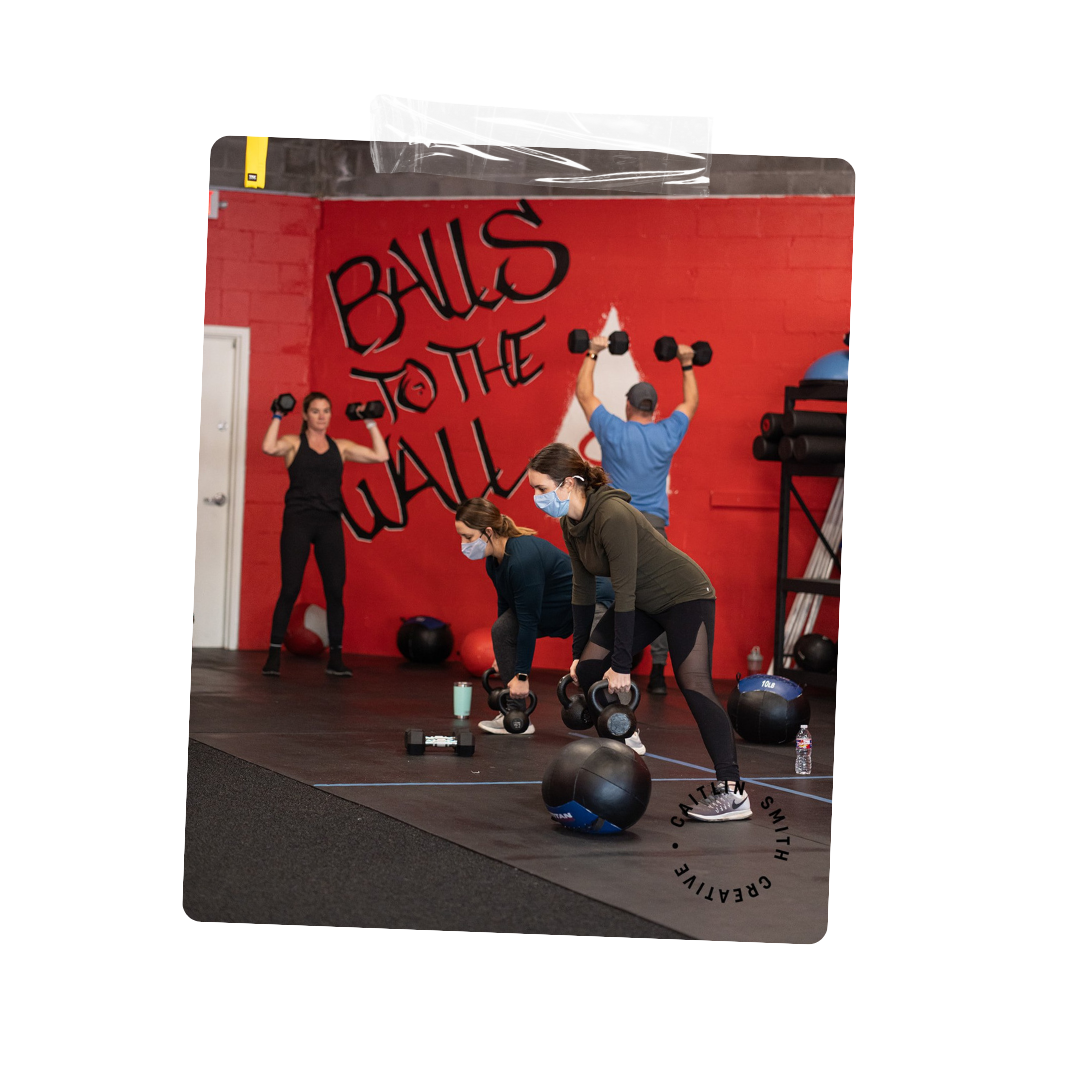 People working out in a gym with a red wall, lifting dumbbells and wearing masks.