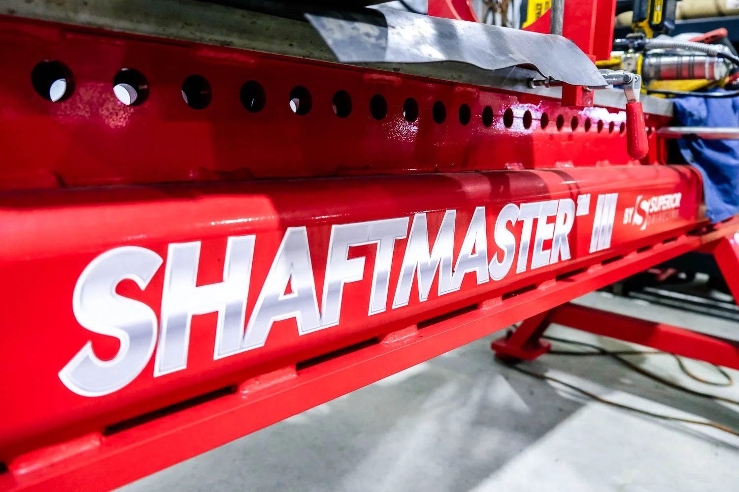 Close-up of a red machine with the words 'SHAFTMASTER' printed in white on the side, in a mechanic shop.