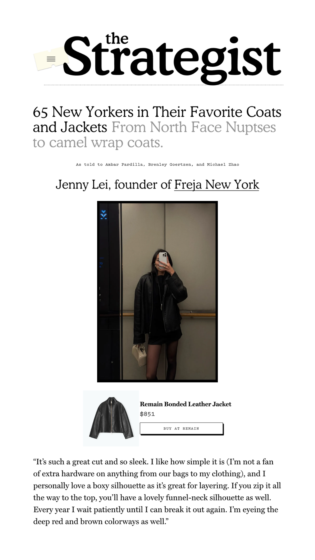 A woman taking a mirror selfie wearing a black leather jacket, black dress, and black tights, holding a beige handbag, standing in an elevator with gray walls and wooden handrails.