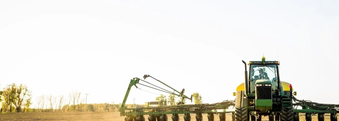 A green tractor operating a large agricultural sprayer in a field during daytime.