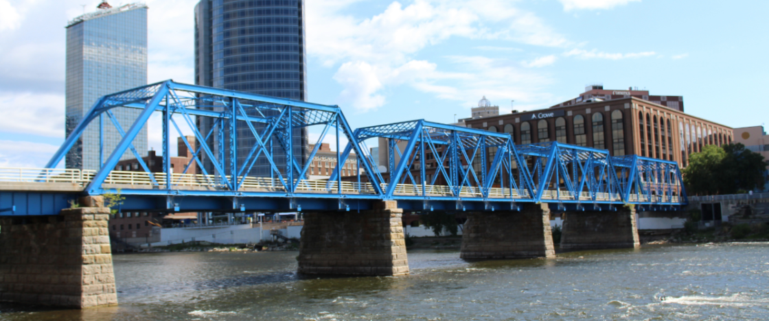 A blue truss bridge over a river in an urban cityscape with high-rise buildings.