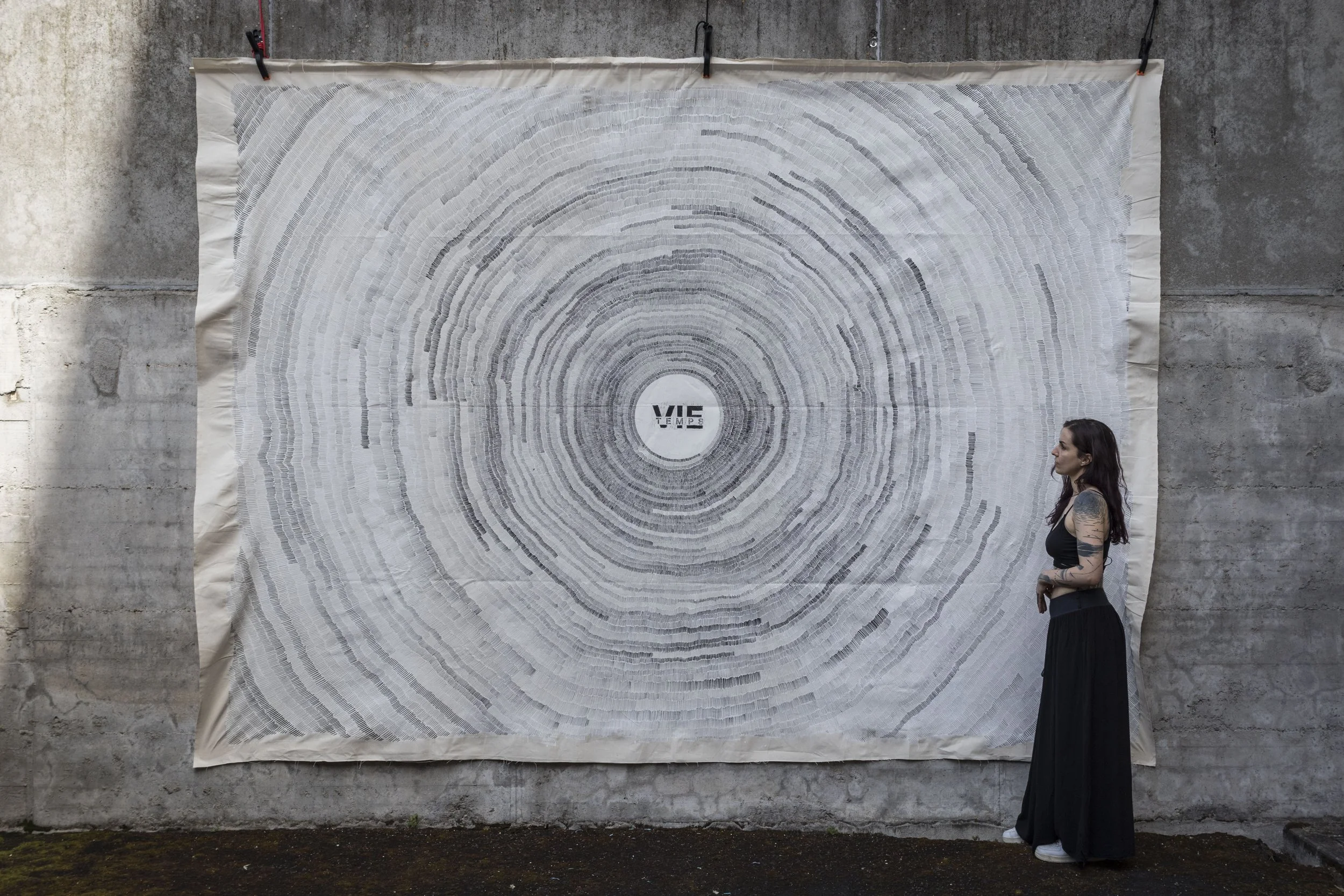 Caroline et "Un trait une seconde". Une performance sur toile qui cumule 86400 secondes. Cette toile est un symbole de perseverance, d'intérêt pour la thématique du temps et de goût prononcé pour les compositions abstraites et géométriques. Caroline 
