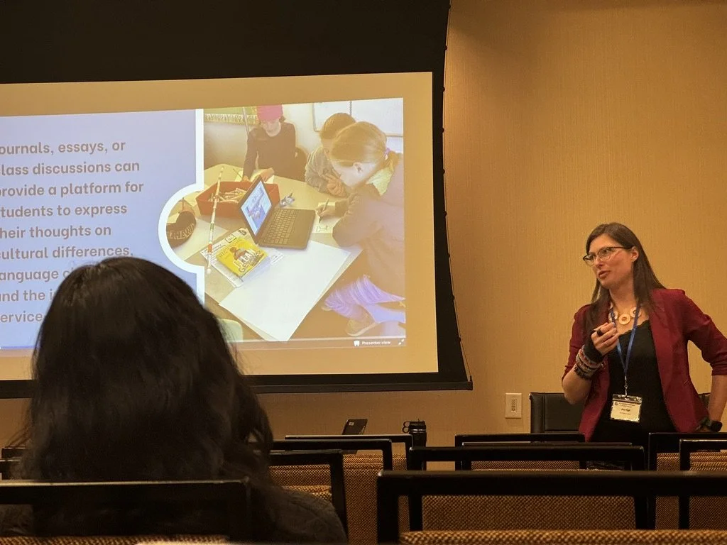 The author giving a presentation in a conference room, with a slide projected behind her showing students gathered around a table with a laptop and school supplies.