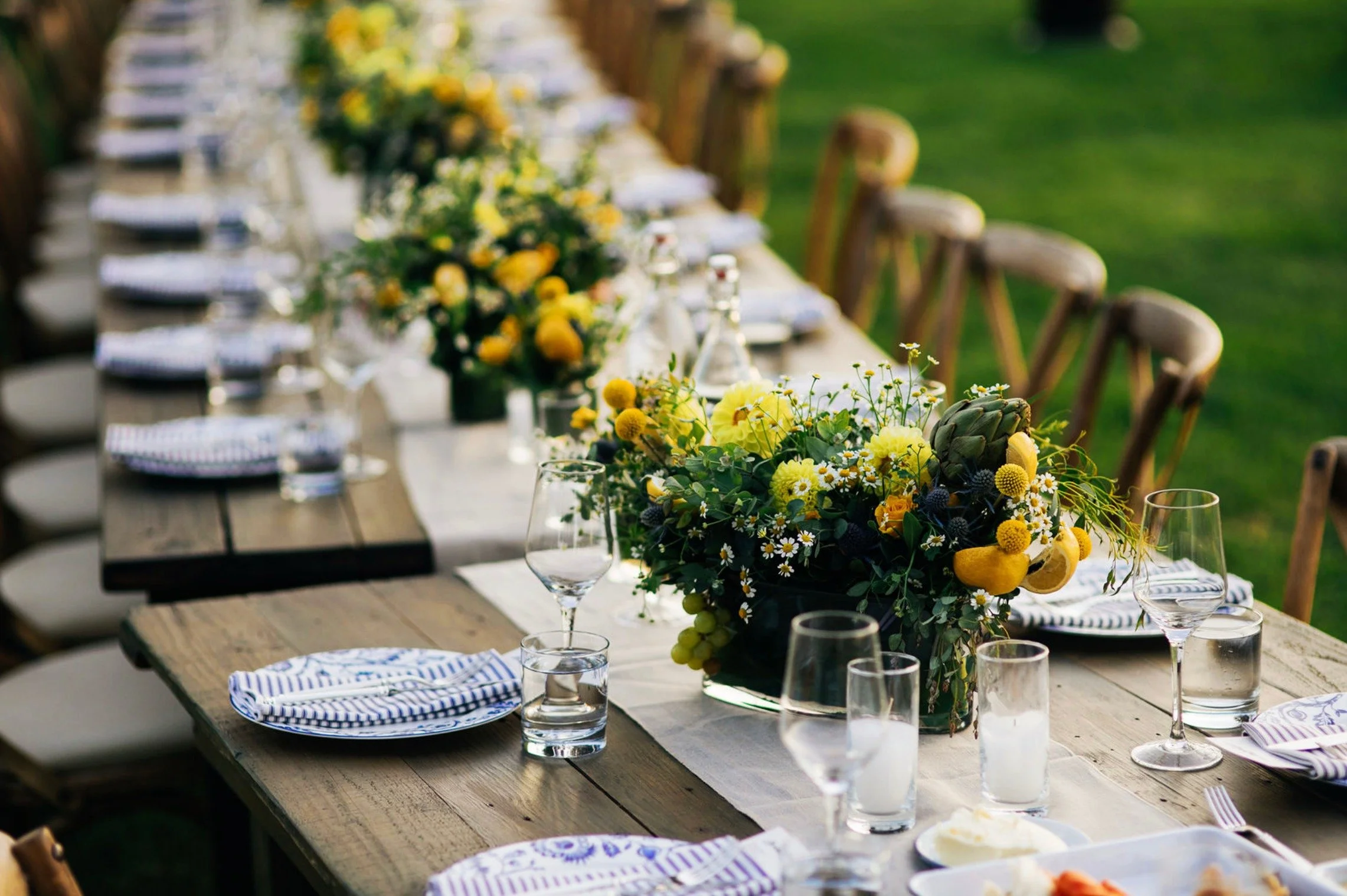 Outdoor farm table with yellow floral centerpieces at luxury summer event — Grove Projects
