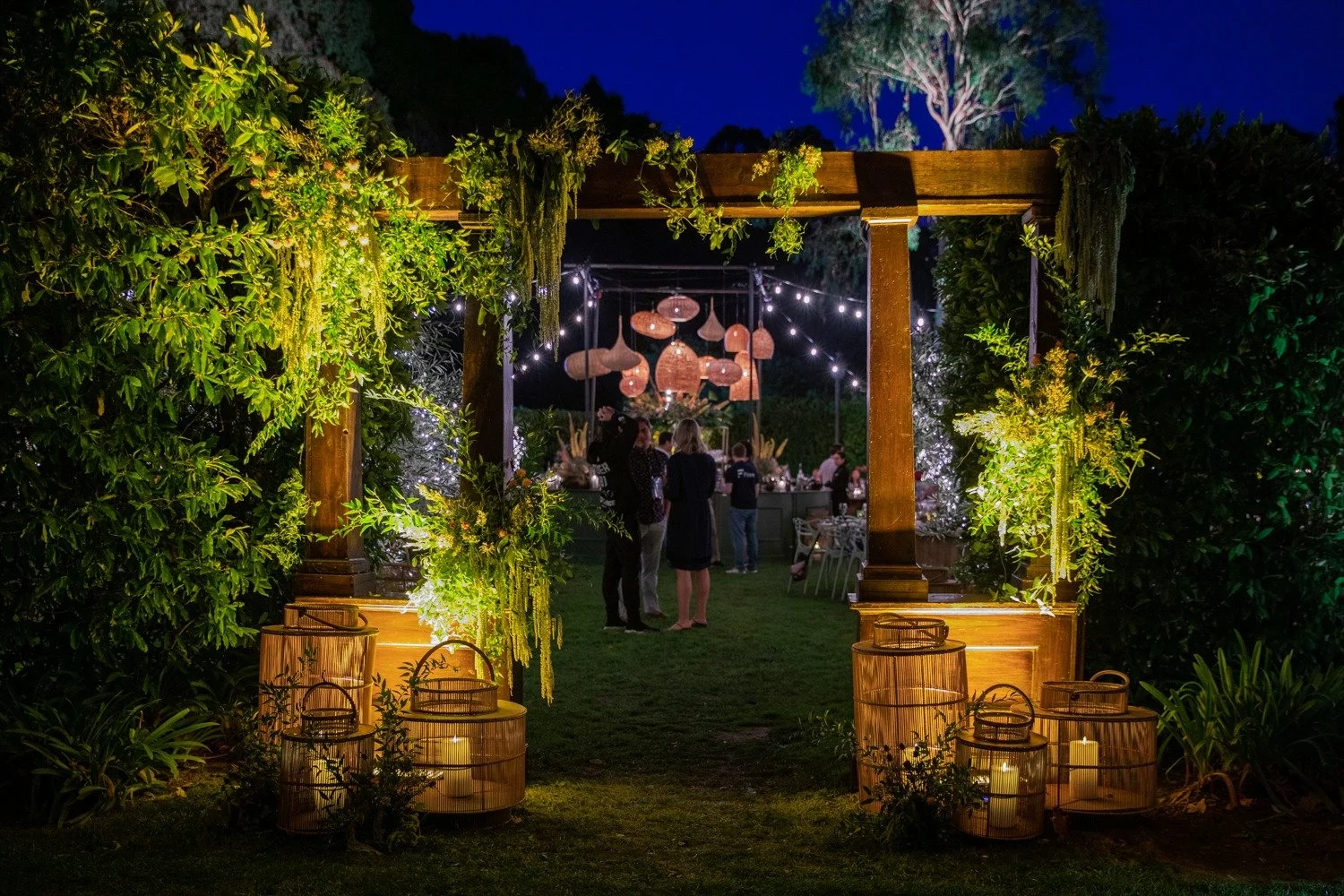 Illuminated outdoor garden event entrance with floral arch and string lights — Grove Projects