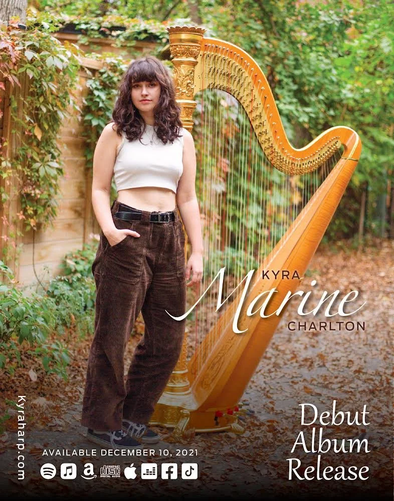 Young woman with curly dark hair in a white sleeveless crop top and brown corduroy pants standing outdoors next to a golden harp with green foliage background, promoting Kyra Marine Charlton's debut album released December 10, 2021.