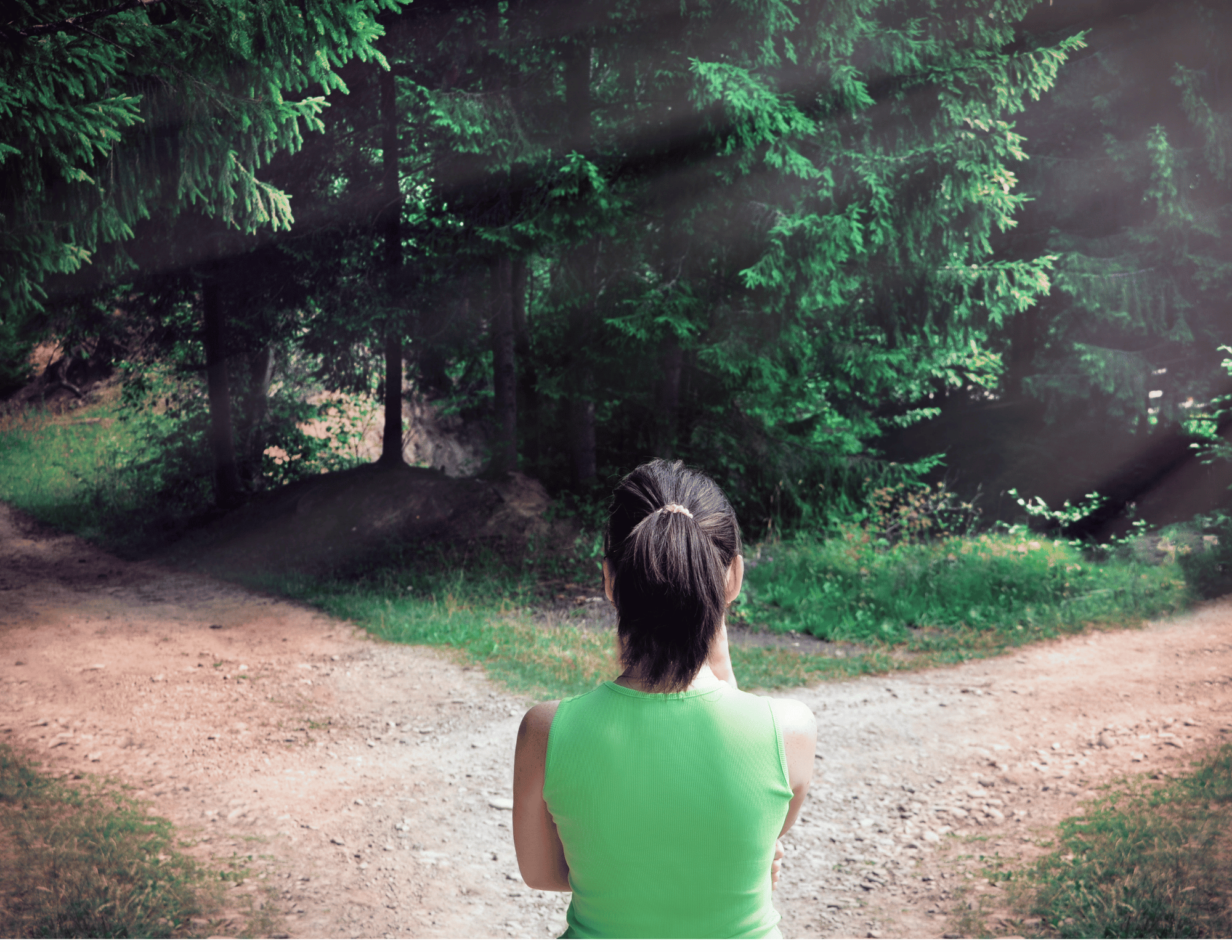 A woman in a green vest with her back to the camera, looking out at a dirt trail in the woods