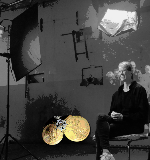 A woman sitting on a chair in a photography studio with lighting equipment, two gold medals on, and a large softbox overhead.