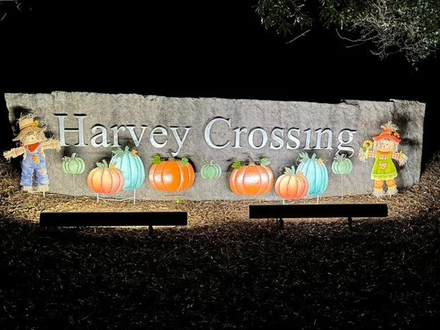 Sign that reads 'Harvey Crossing' with fall-themed decorations including pumpkins and scarecrows.