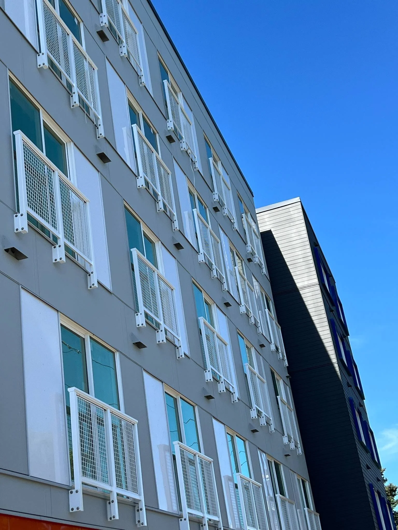 Side view of a modern multi-story building with numerous windows and white balcony railings under a clear blue sky.