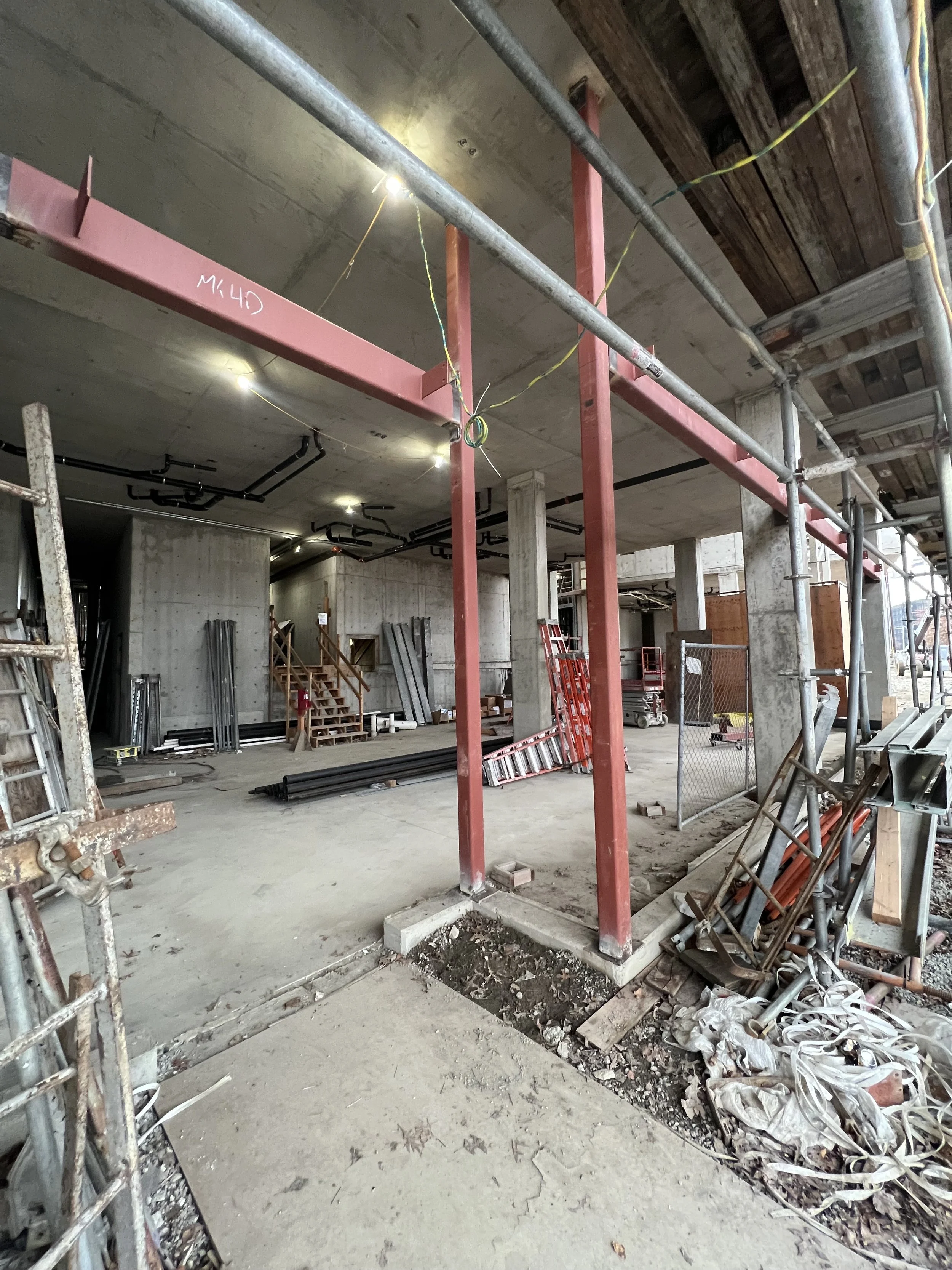 Construction site inside a building with scaffolding, construction materials, and unfinished walls and ceiling.