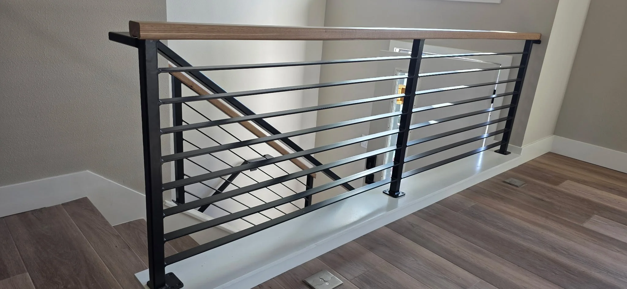 Metal and wood staircase railing in a modern home, with wood flooring and light-colored walls.