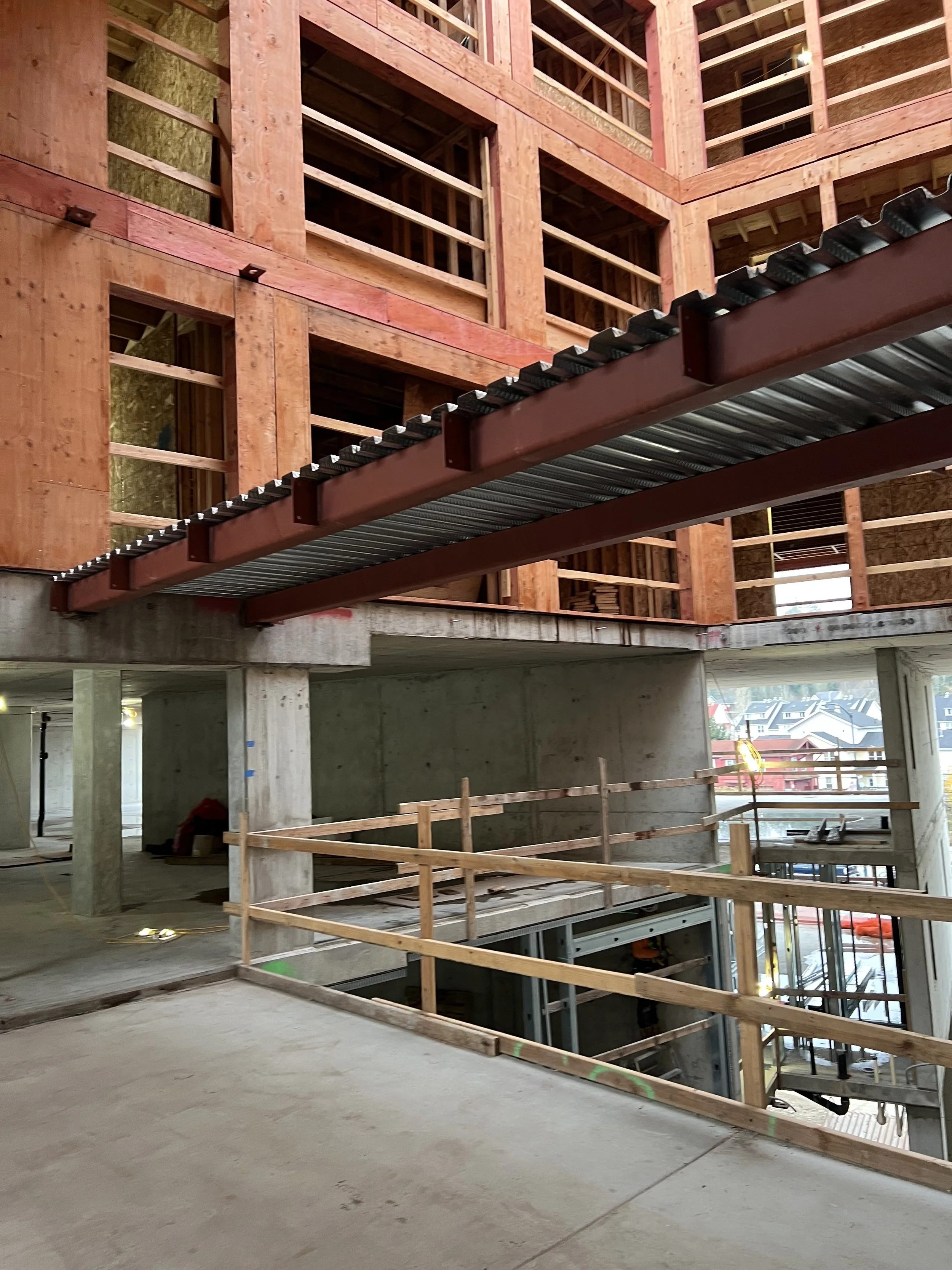 Interior view of a building under construction, showing wooden framing, a concrete floor, and a steel support beam with a corrugated metal deck.