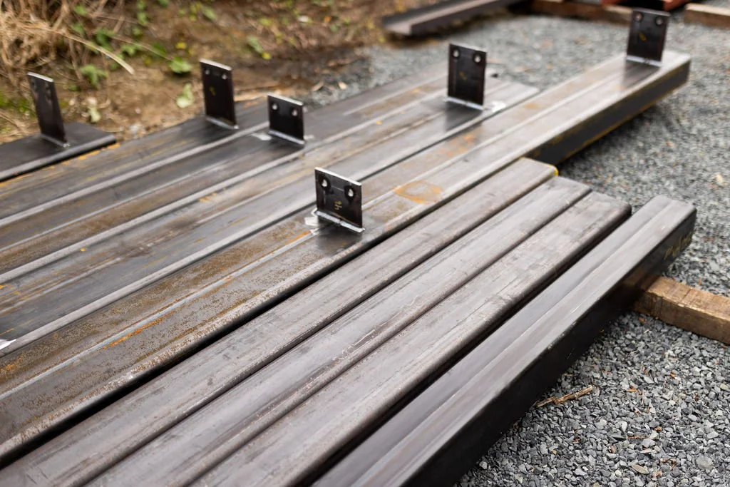 View of a wooden deck under construction with metal brackets attached, laid on a gravel surface.
