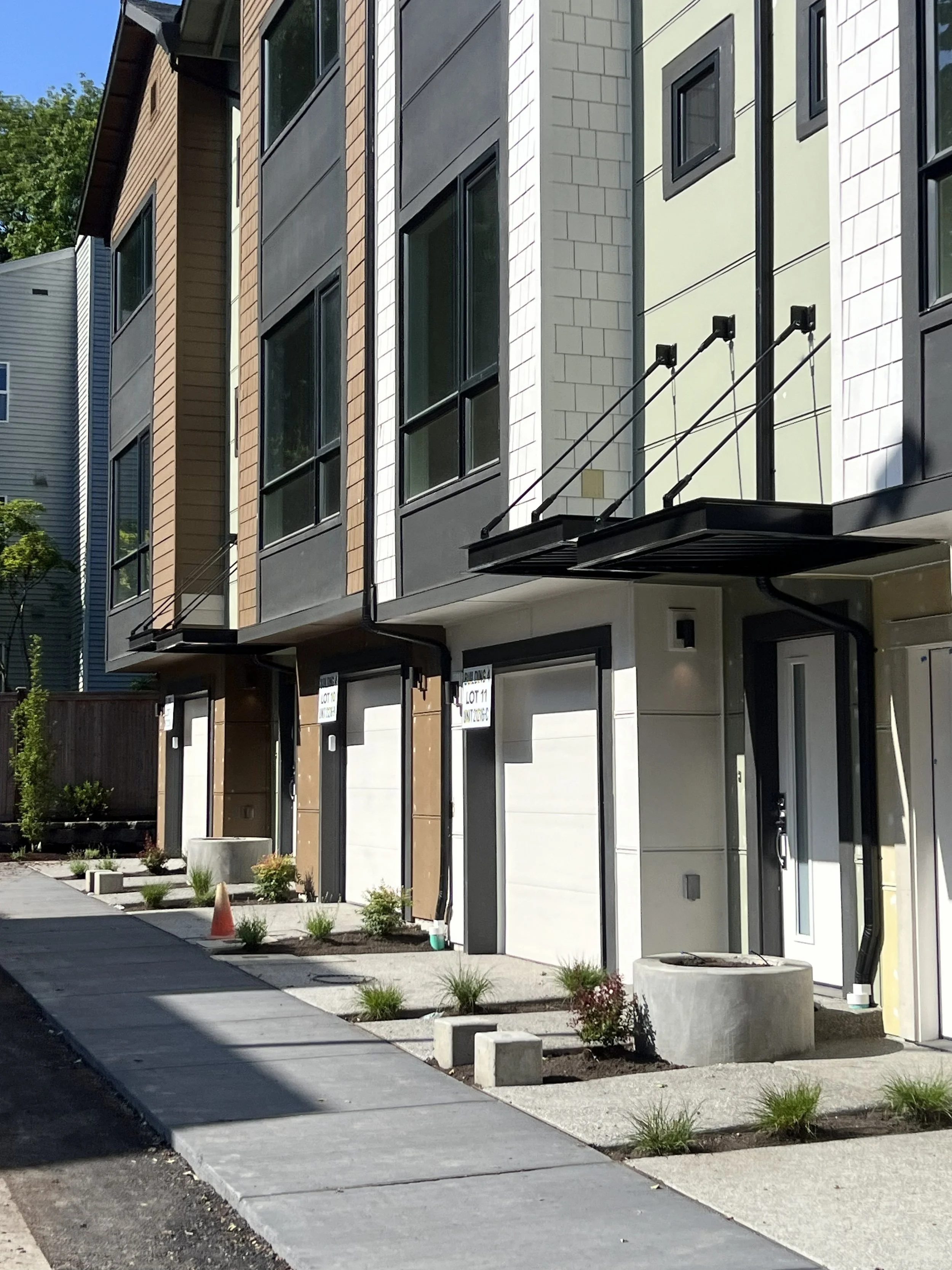 Construction site of new row of modern townhouses with varying exterior finishes, small front yard landscaping, and concrete walkways.