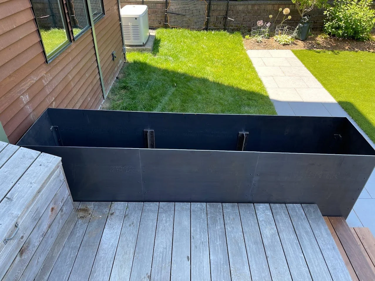 Backyard with grass, patio tiles, and a wooden deck with a metal planter box.