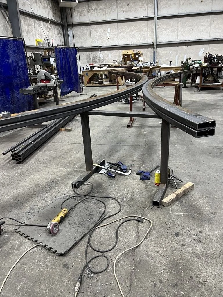 Metal curved track or rail on supports in a workshop with tools and materials scattered around.