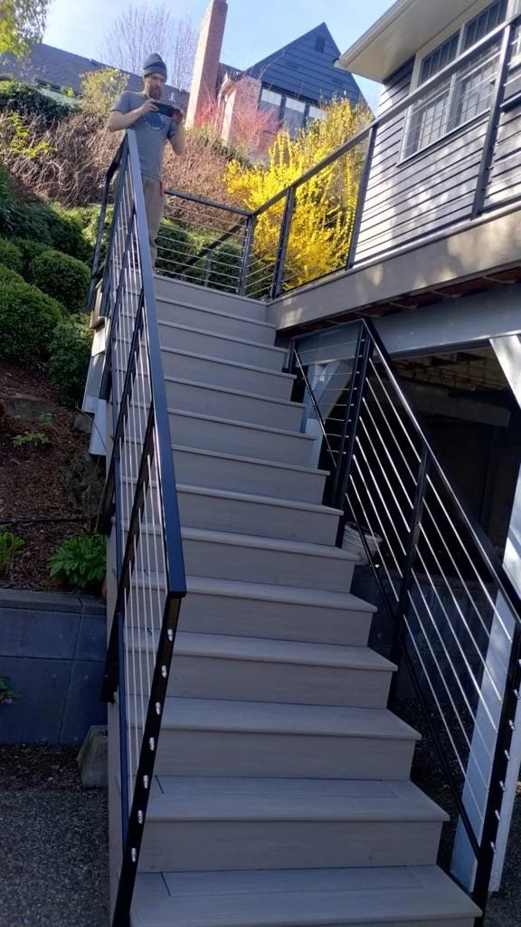 Person standing at the top of an outdoor staircase, looking at a device, with a garden and house in the background.