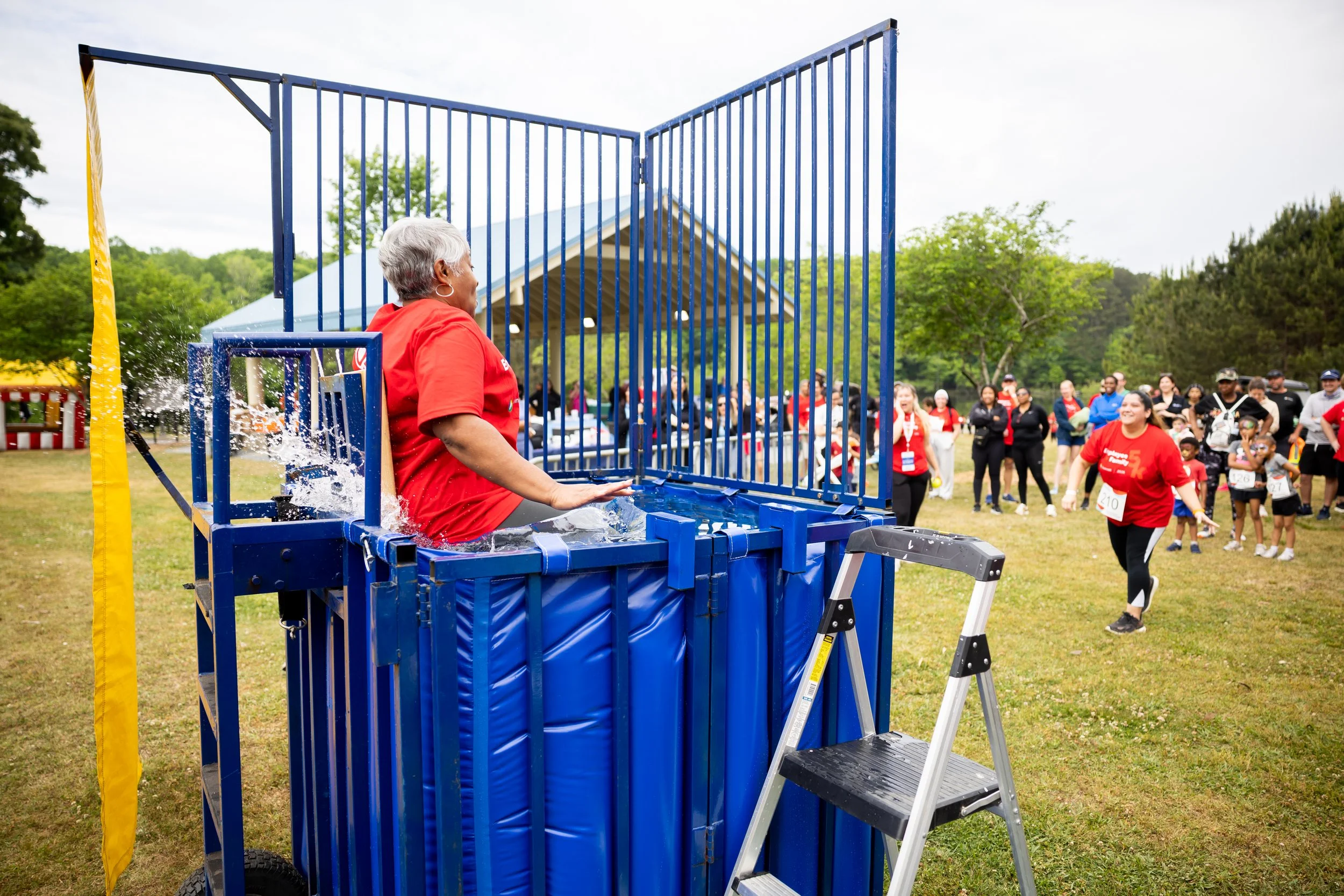 Woman sitting on a water slide at an outdoor event with people gathered around.