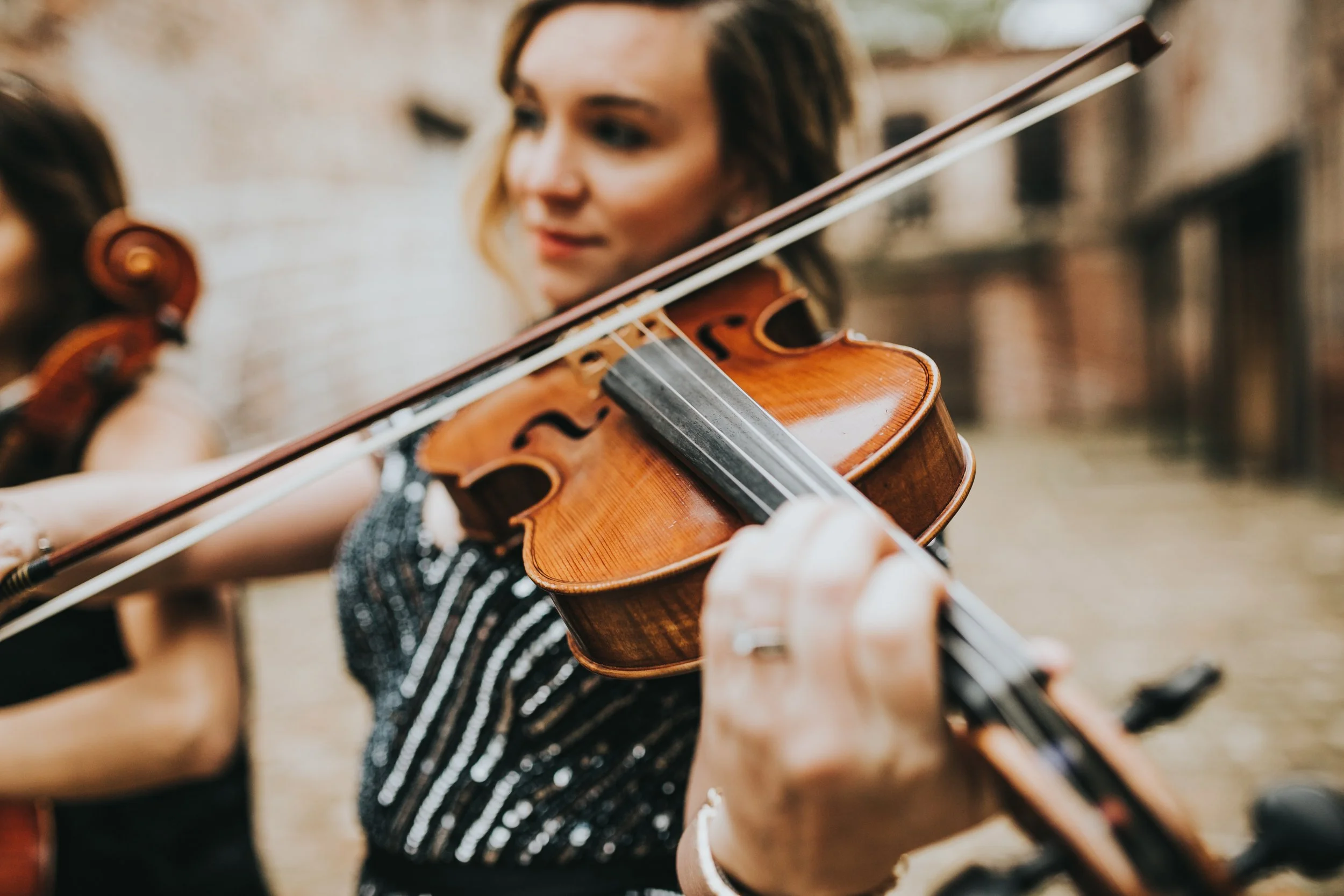 A woman playing the violin outdoors, with a focus on her face and the instrument.