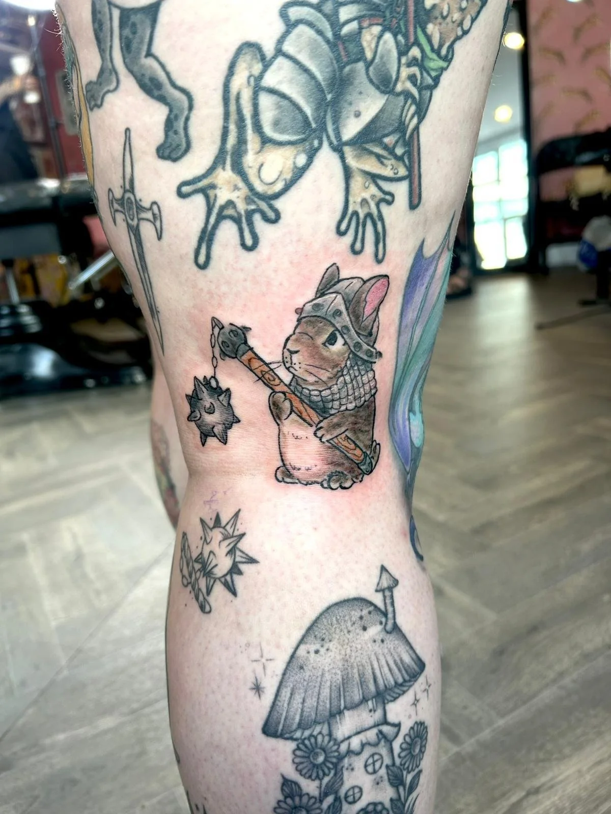 Tattoo of a hamster dressed as a Viking, holding a mace, with a large dragonfly above, and other smaller tattoos of a mushroom house, a fox face, and a star.