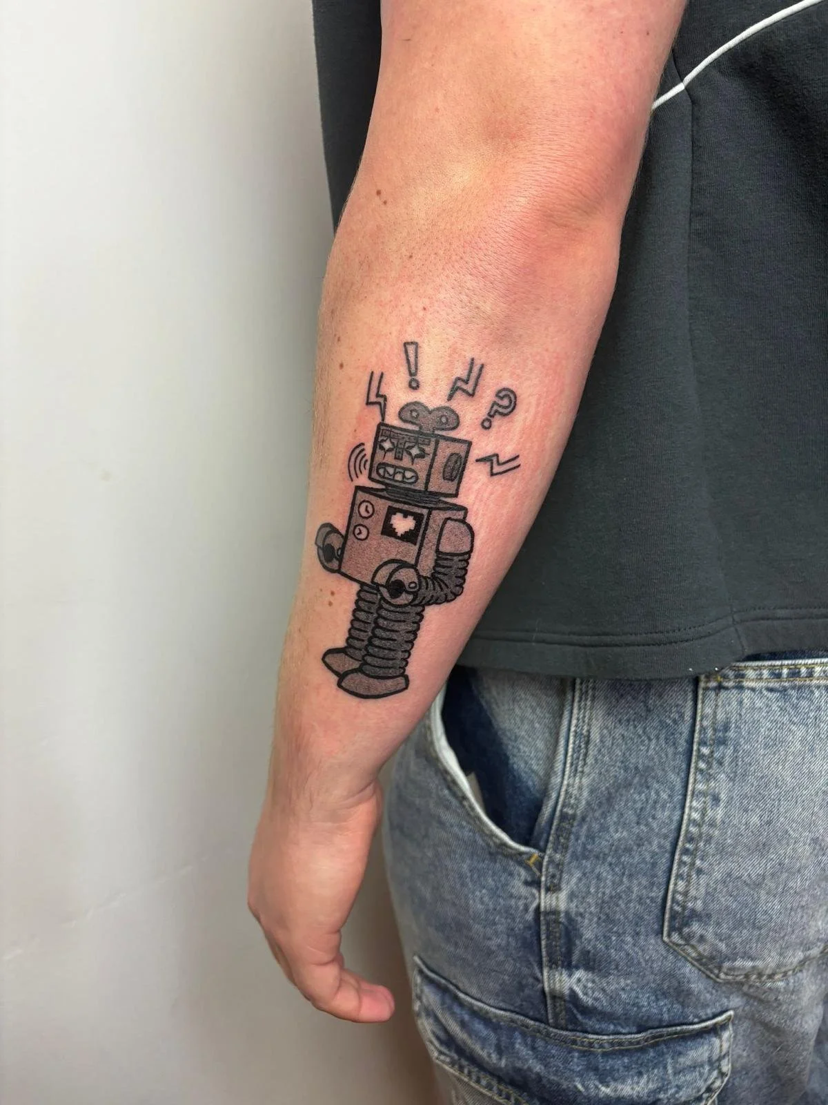 Tattoo of a cartoon robot on person's forearm, with geometric shapes and symbols above its head.