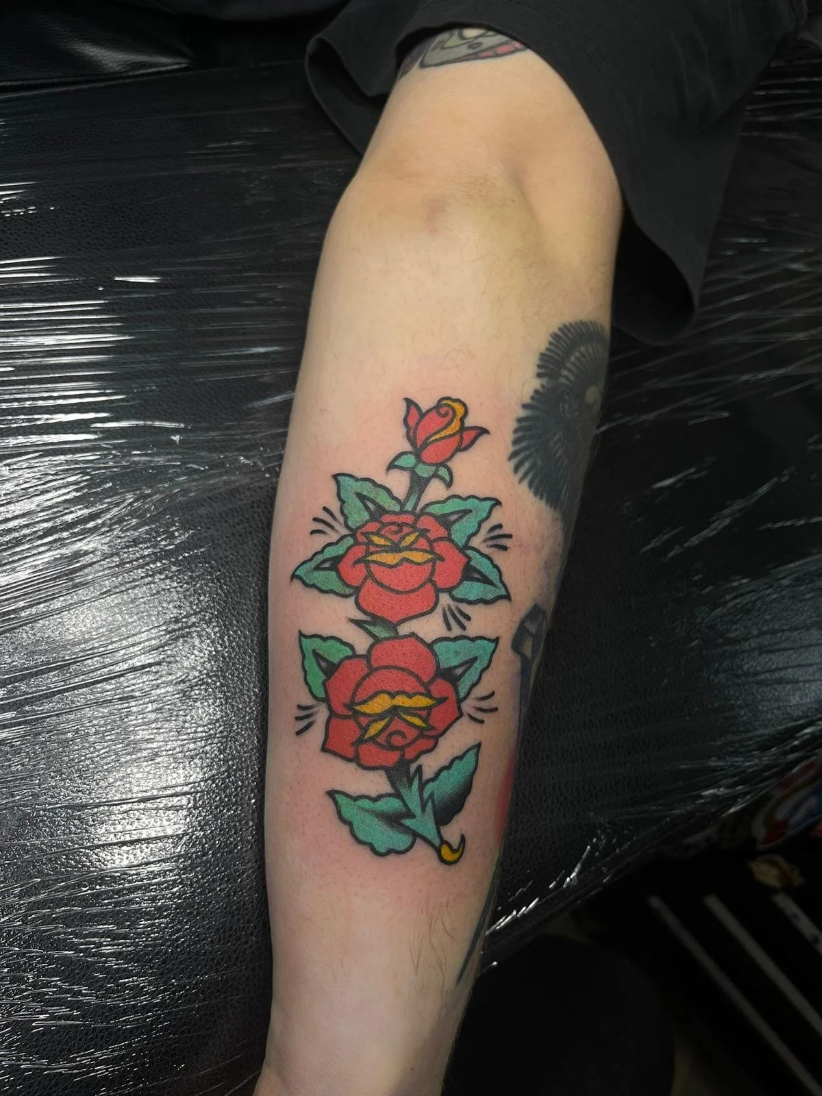 Tattoo of three red roses with green leaves on a person's forearm.