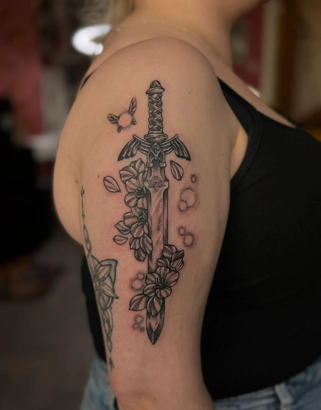 Black and gray tattoo of a sword surrounded by flowers on a person's upper arm.