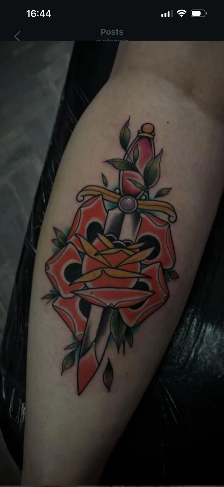 Colorful tattoo of a dagger piercing through a red flower with green leaves.