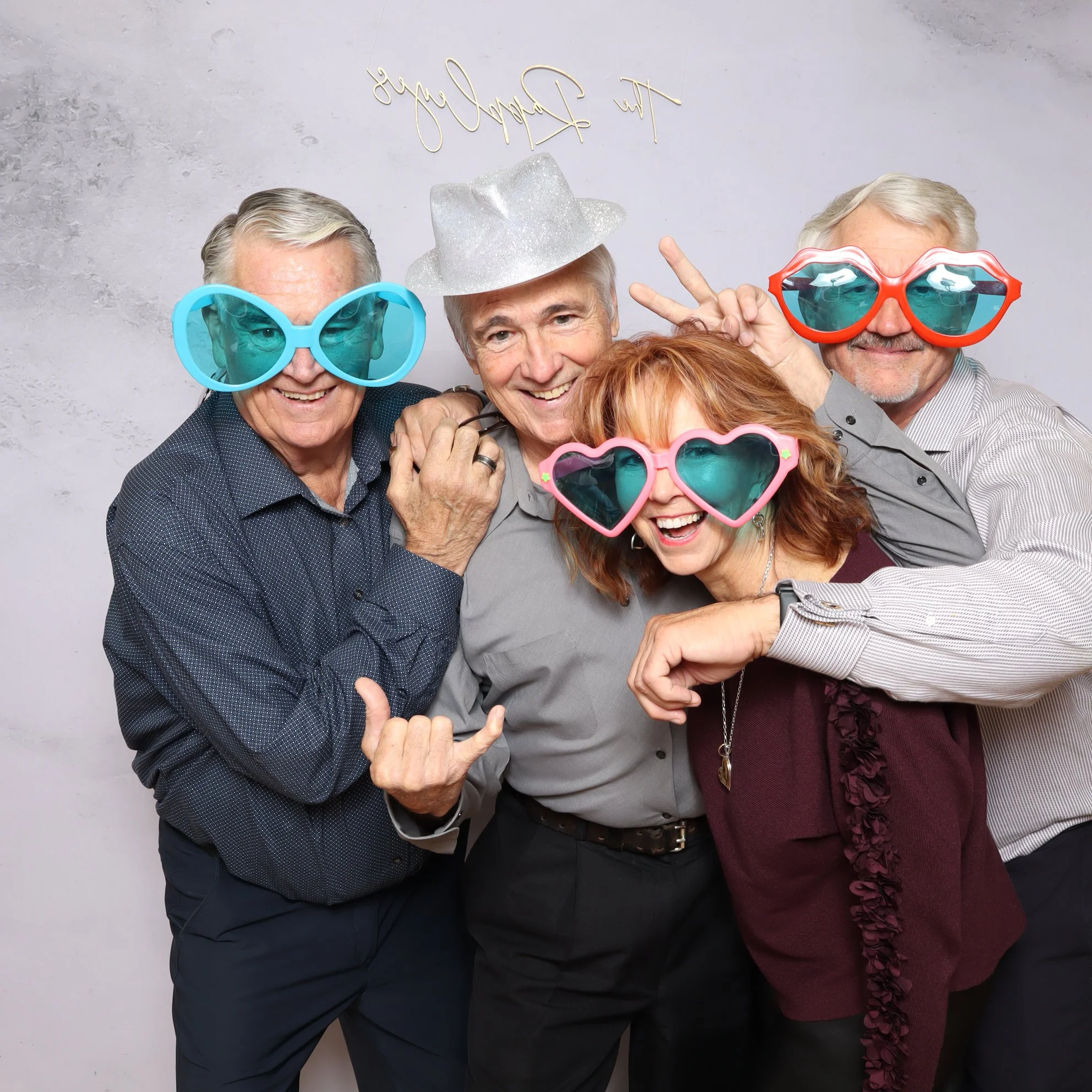 Four seniors wearing colorful sunglasses and silly accessories, smiling and posing for a fun photo.