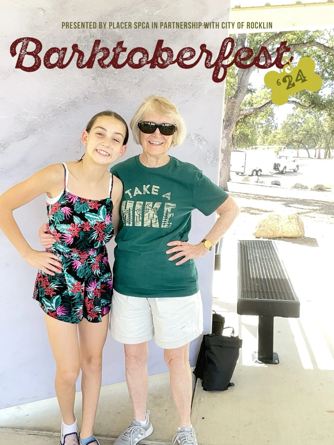 A young woman and an older woman smiling and standing side by side outdoors with a bench and trees in the background. The young woman is wearing a floral tank top and shorts, and the older woman is wearing sunglasses, a green t-shirt with 'Take a Hike' printed on it, and white shorts.