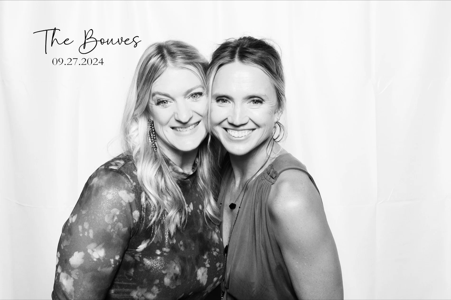 Black and white photo of two women smiling, standing close together with the woman on the left wearing a floral dress and the woman on the right wearing a sleeveless top. Text in upper left corner reads 'The Bouvens' with the date '09.27.2024' underneath.