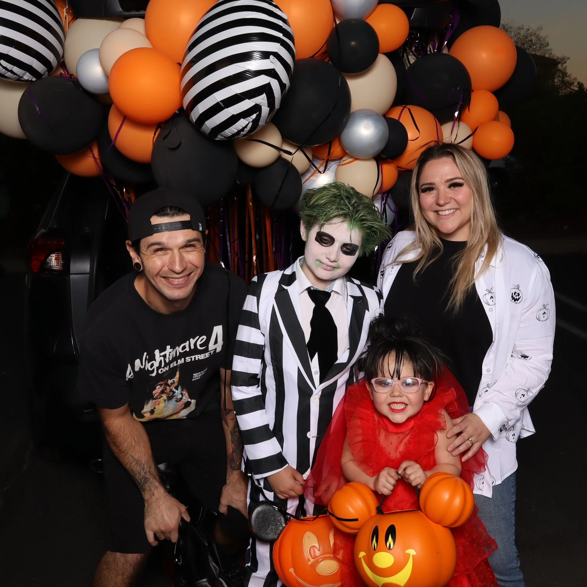 A group of four people in Halloween costumes posing in front of a large Halloween-themed balloon display.