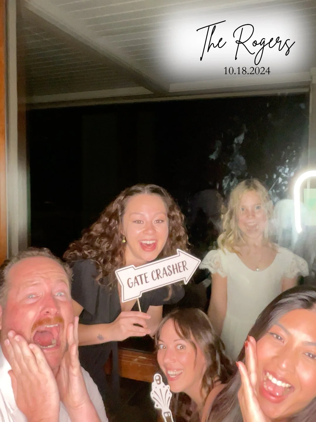 Group of five people posing in a photo booth at an event, with some holding props and signs. One person is holding a sign that says 'Gate Crasher'. The top right corner shows text that reads 'The Rogers 10.18.2024'.