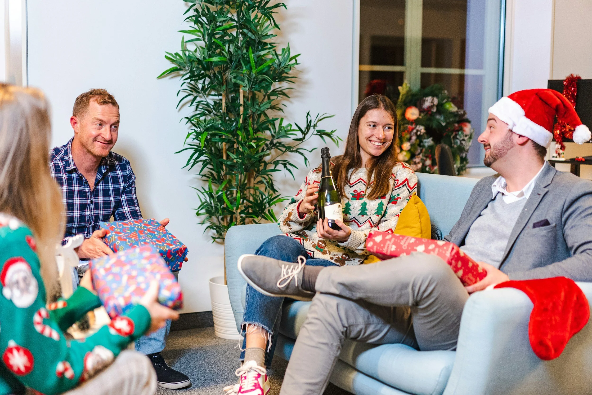 Four employees sitting in a circle with Christmas decorations and exchanging gifts in front of a Tangerine Photo Booth.