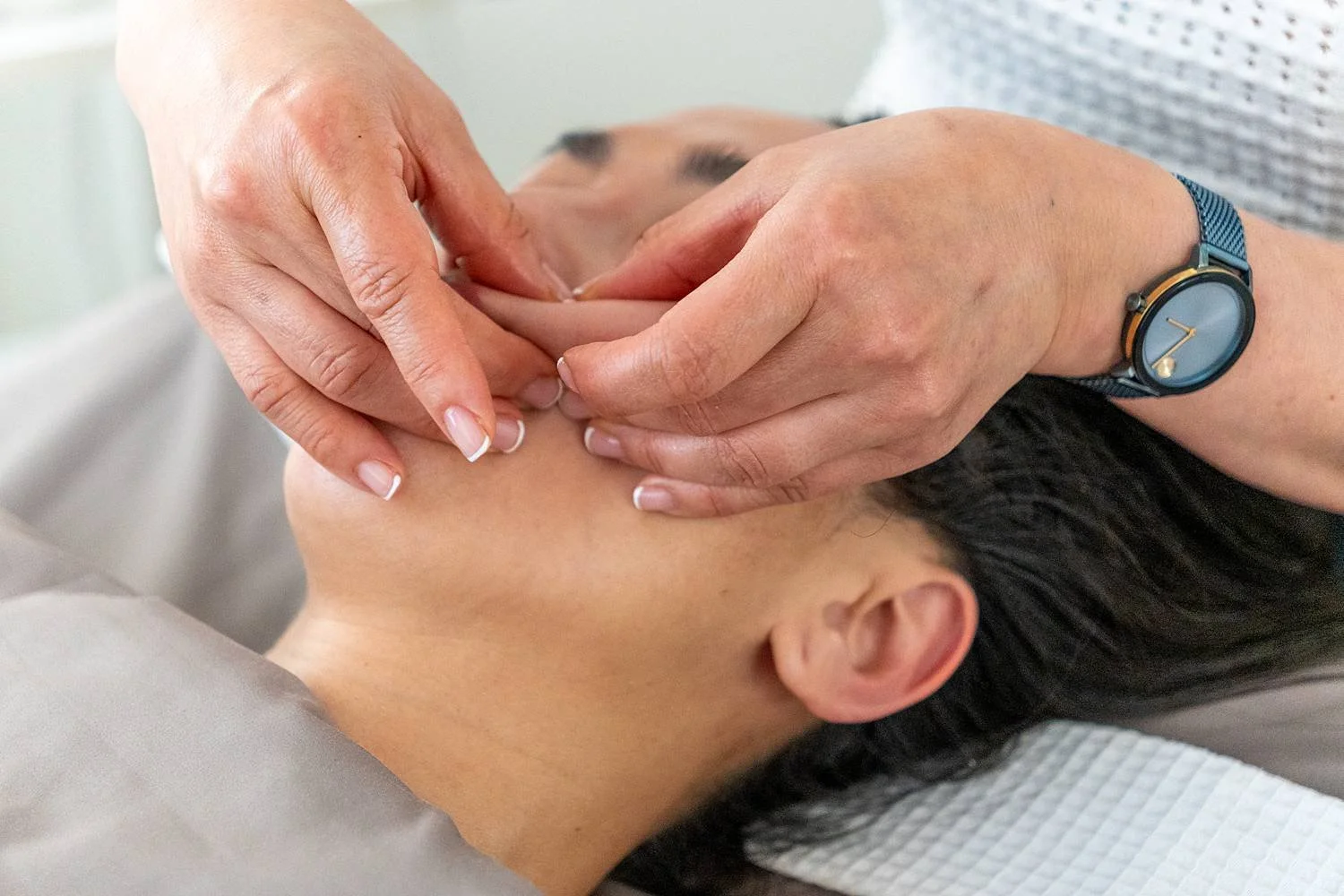 A person receiving acupuncture treatment on the neck with thin needles inserted, while lying down.