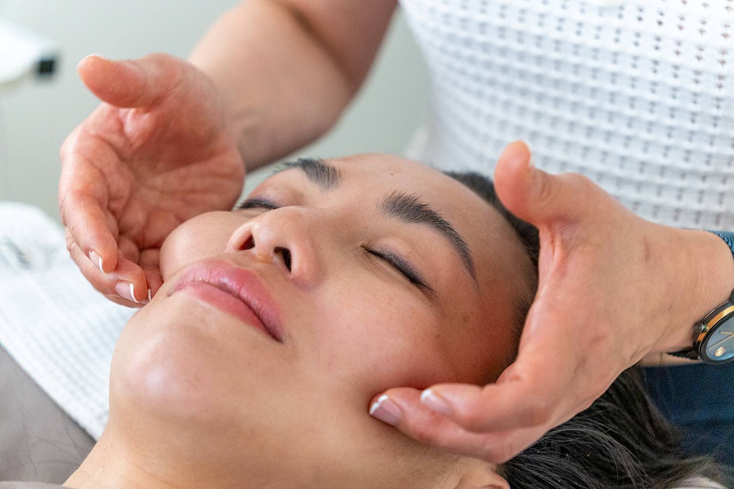 Person receiving facial treatment from a therapist, who is gently massaging their face with both hands.