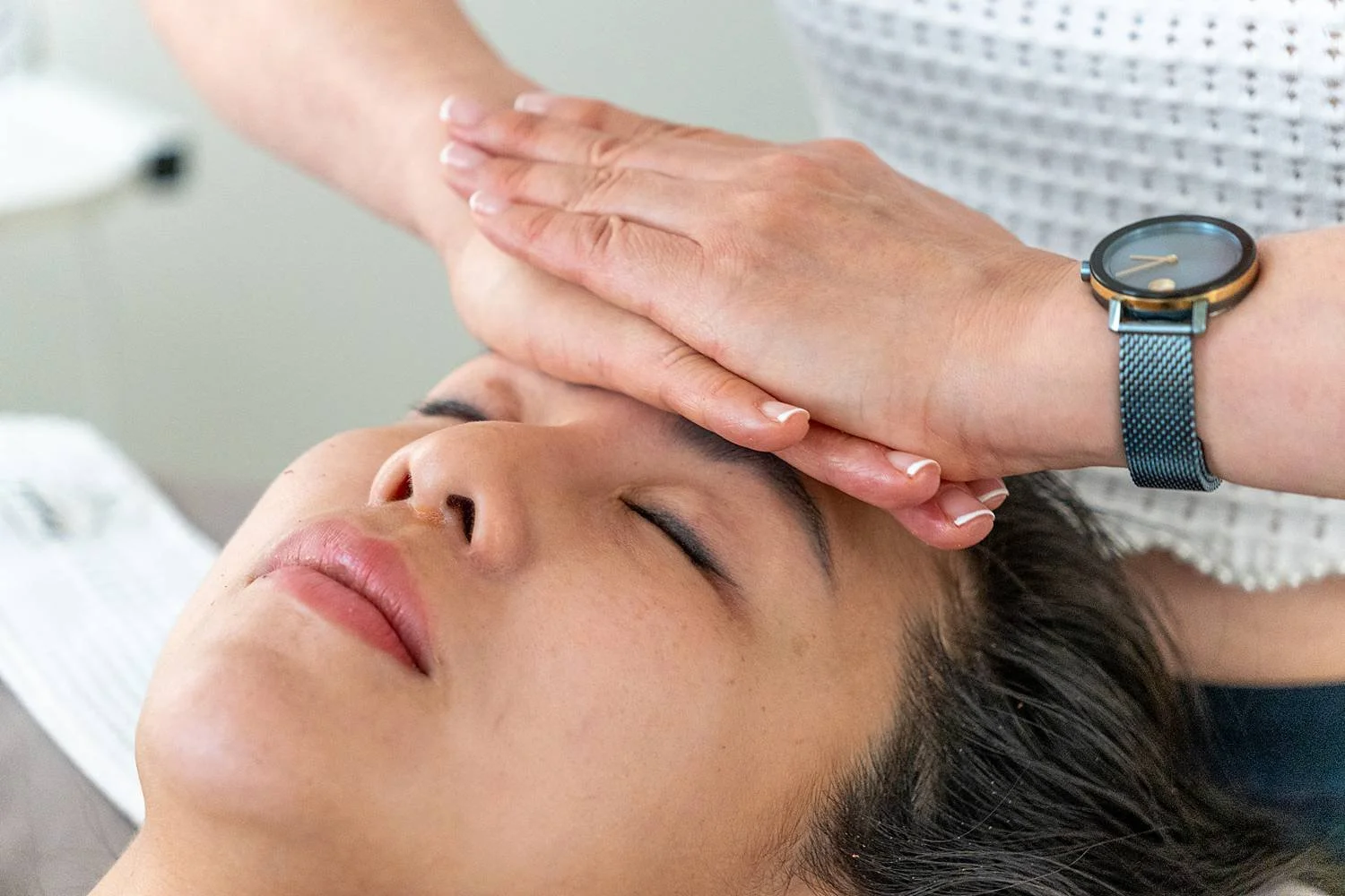 A person receiving a facial massage from a therapist in a spa or clinic setting.