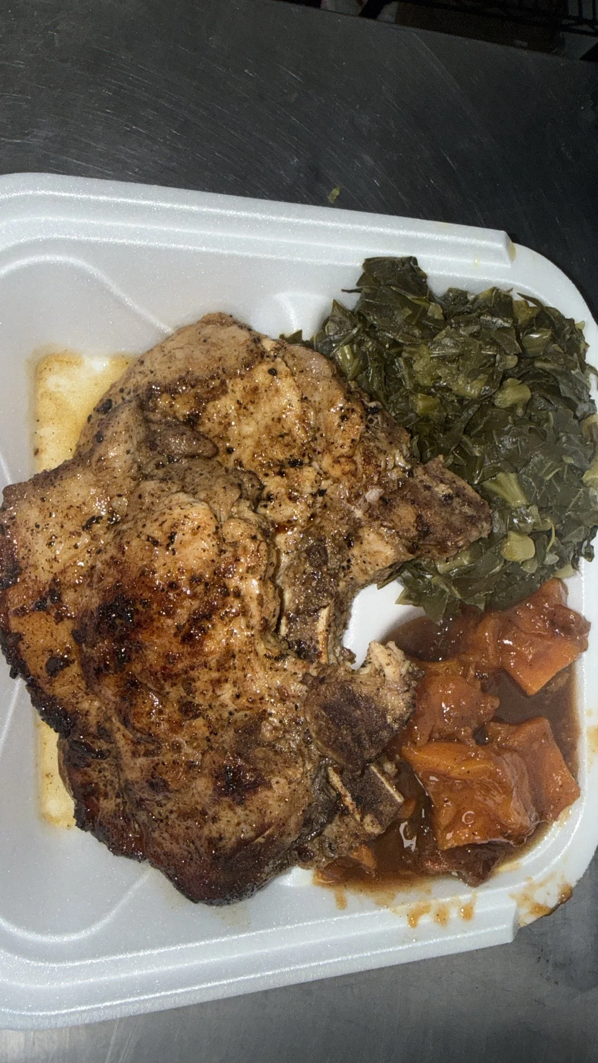 Fried chicken leg with cooked greens and tomato-based vegetable side in a foam takeout container.