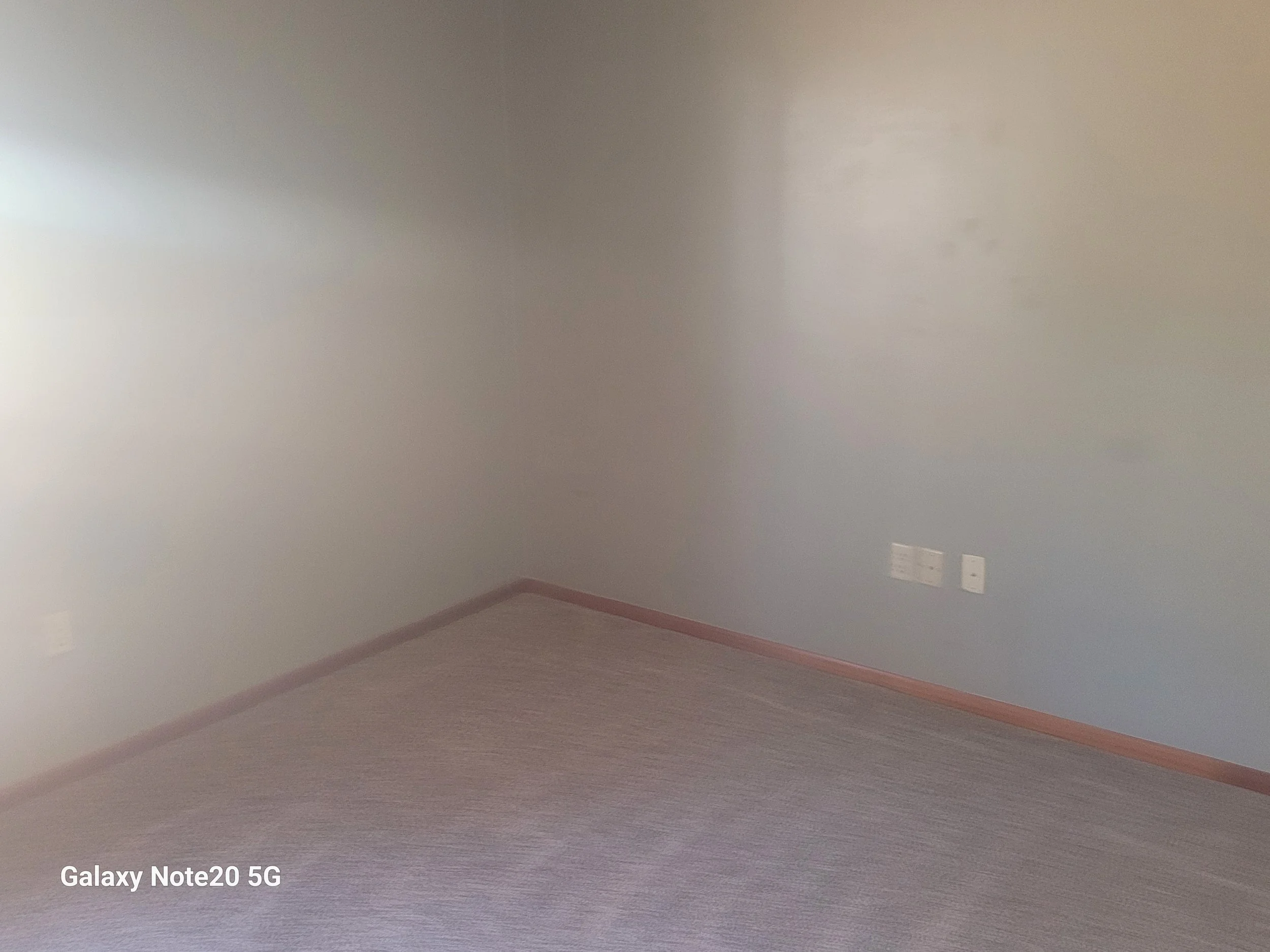 Empty room with beige walls and gray carpeted floor; two electrical outlets on the wall.