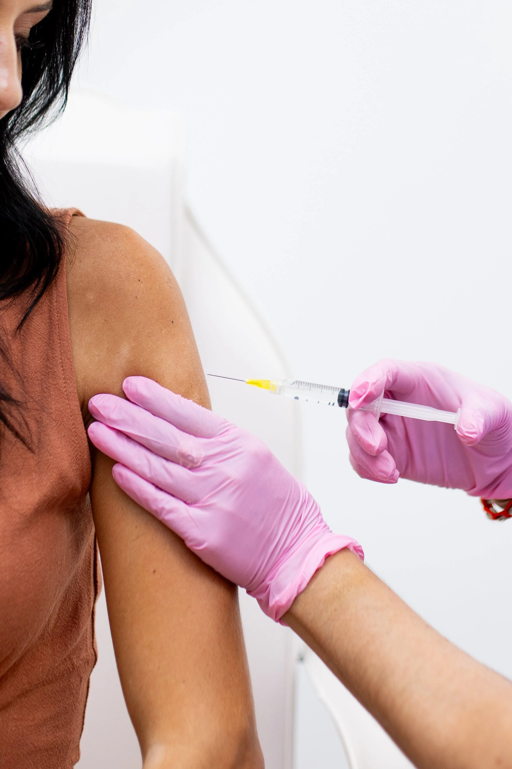 A woman receiving a vaccine shot in her upper arm from a healthcare professional wearing pink gloves.