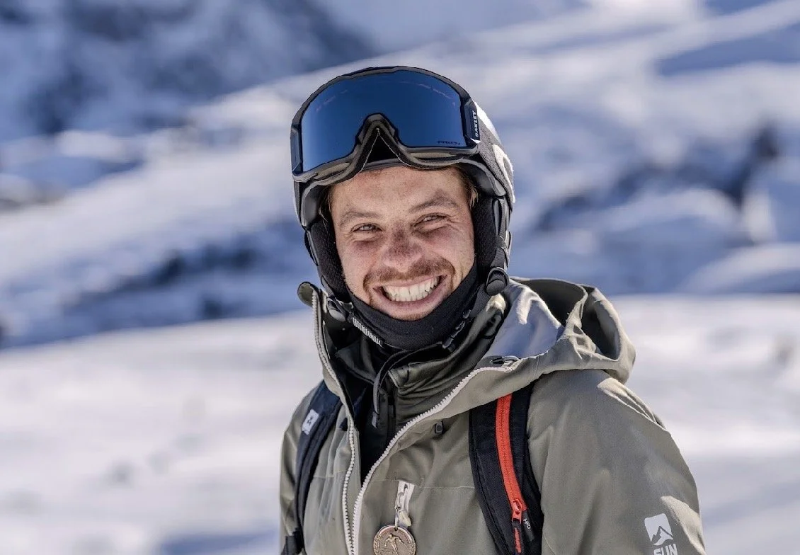 A man wearing ski gear and a helmet, smiling in a snowy mountain landscape in the resort Val Thorens on the 3 Vallées.