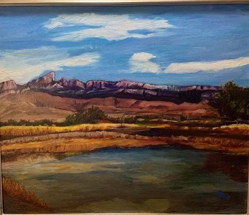 Landscape painting of mountains, blue sky with clouds, and a body of water in the foreground.