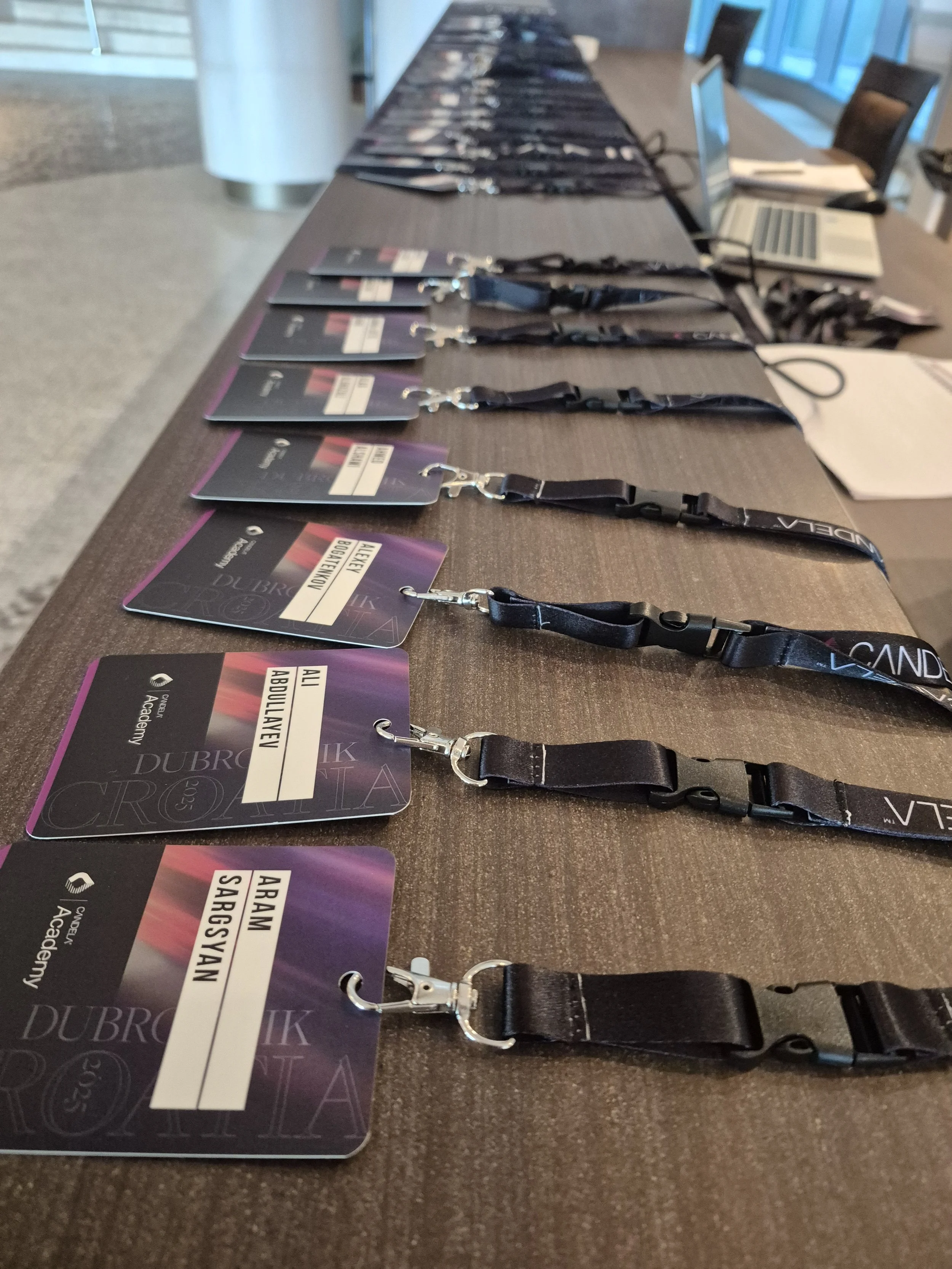Several conference badges with lanyards laid out on a brown table, with laptops and papers in the background.