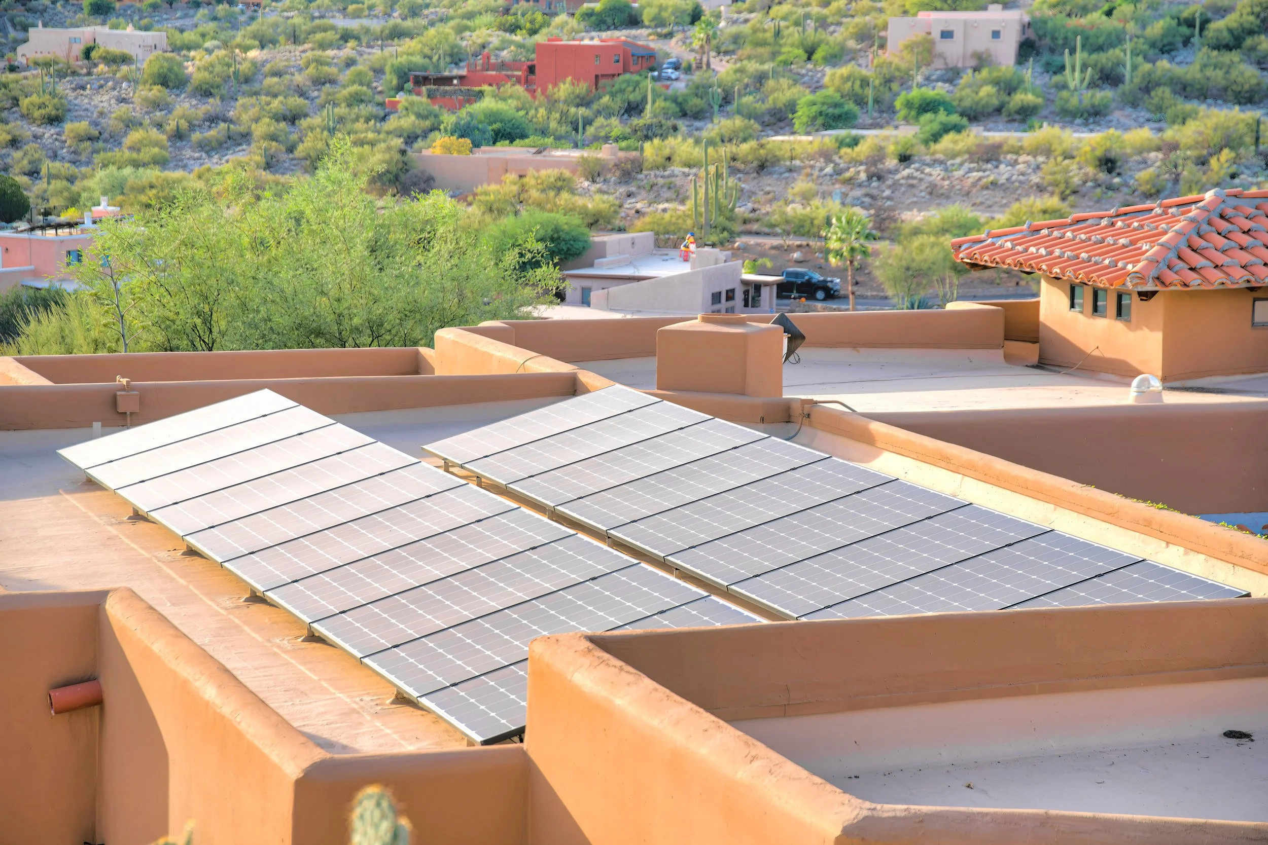 Rooftop with solar panels in a desert landscape with cacti and houses in the background.