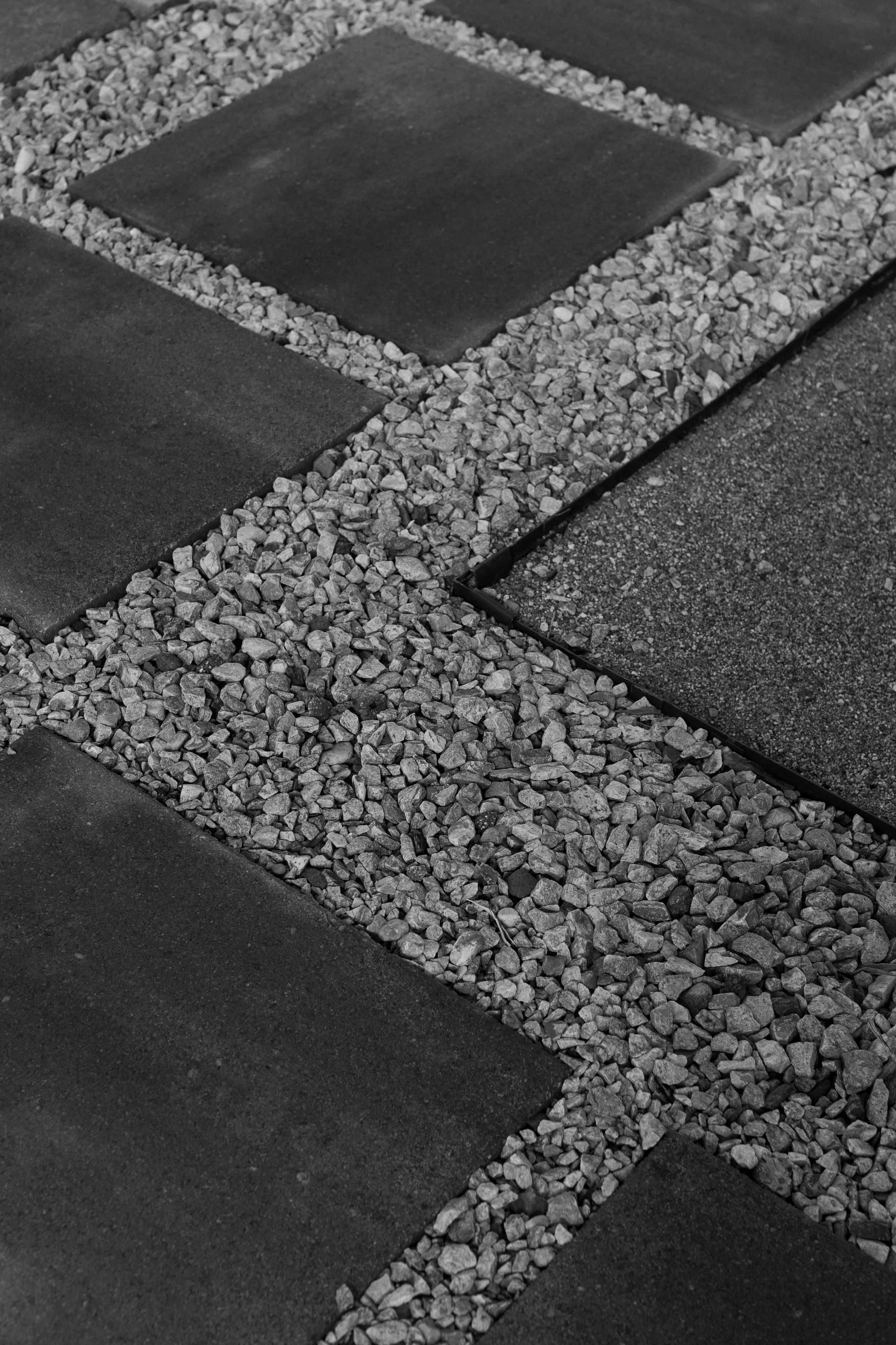A close-up photo of a section of a walkway with square paving stones surrounded by small gravel and bordered by a strip of smoother concrete.
