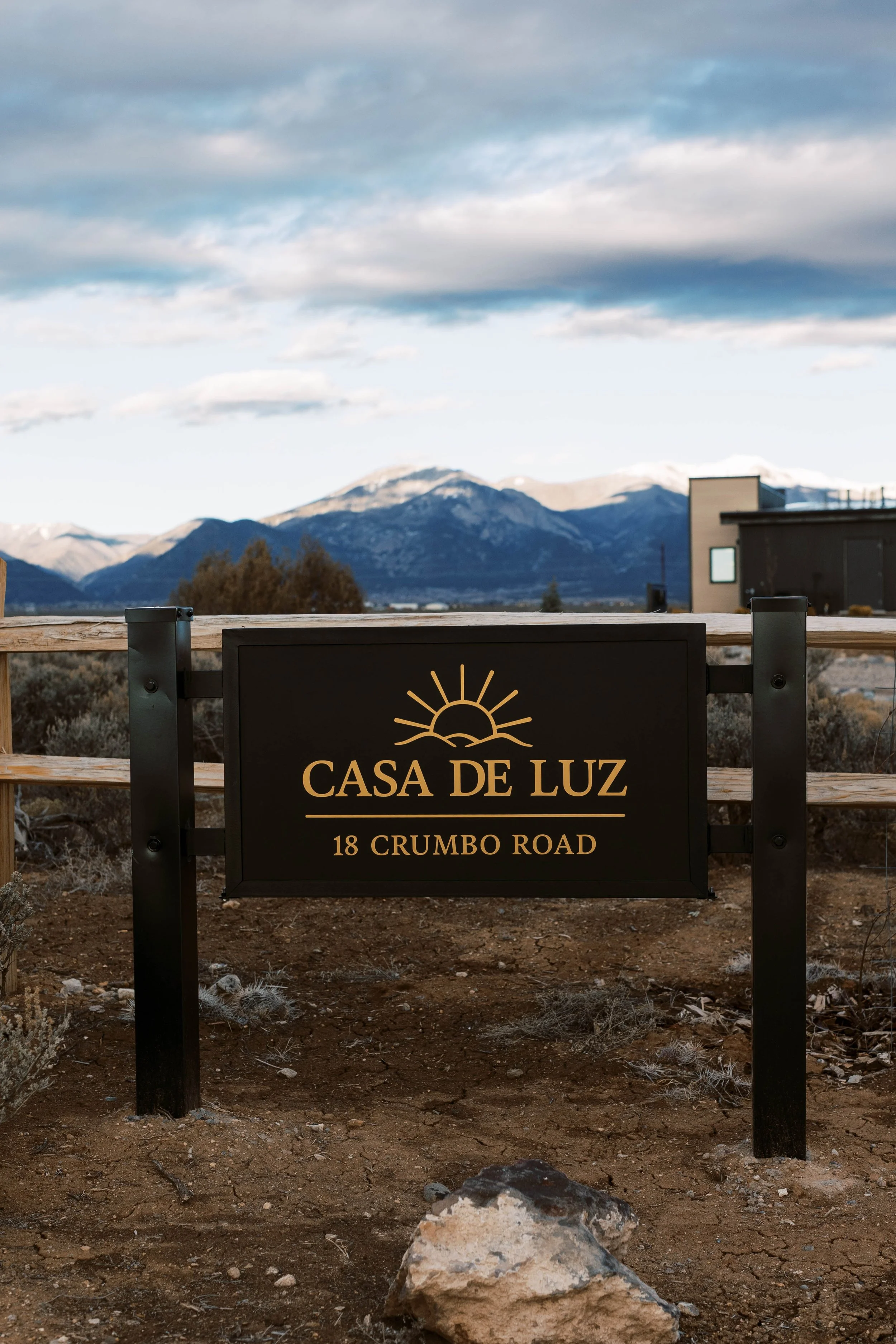 Sign for Casa de Luz at 18 Crumbo Road with mountainous landscape and cloudy sky in the background.