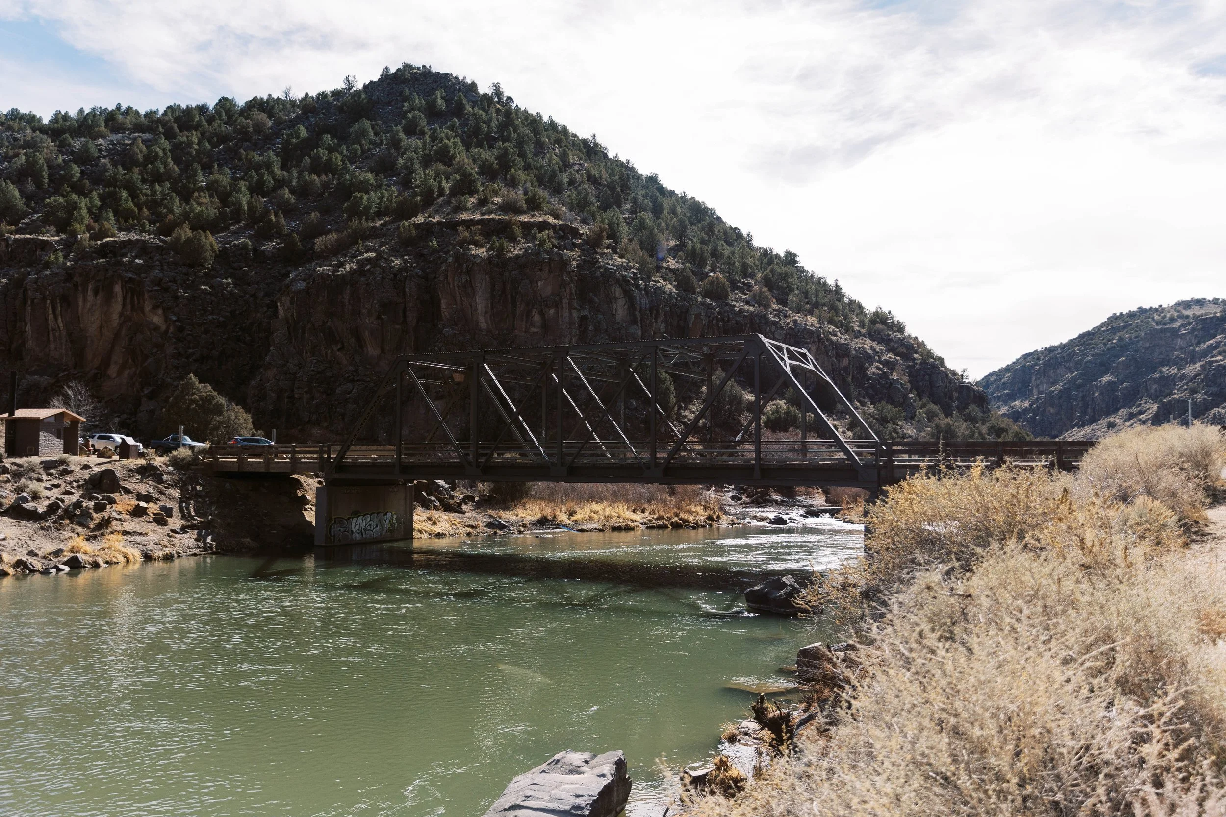 A river flowing through a mountainous landscape with a bridge crossing over it, under a partly cloudy sky.